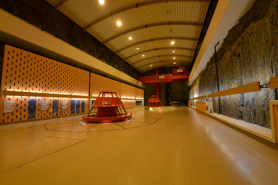 Machine hall with generating units, lighting and bare rock wall.